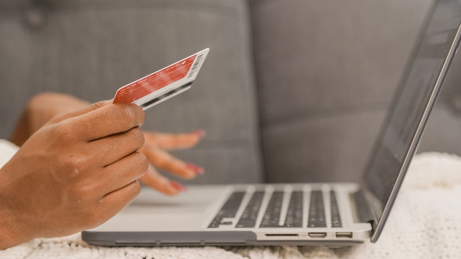 03 ach Personne tenant une carte bancaire devant un ordinateur portable, assise sur un canapé