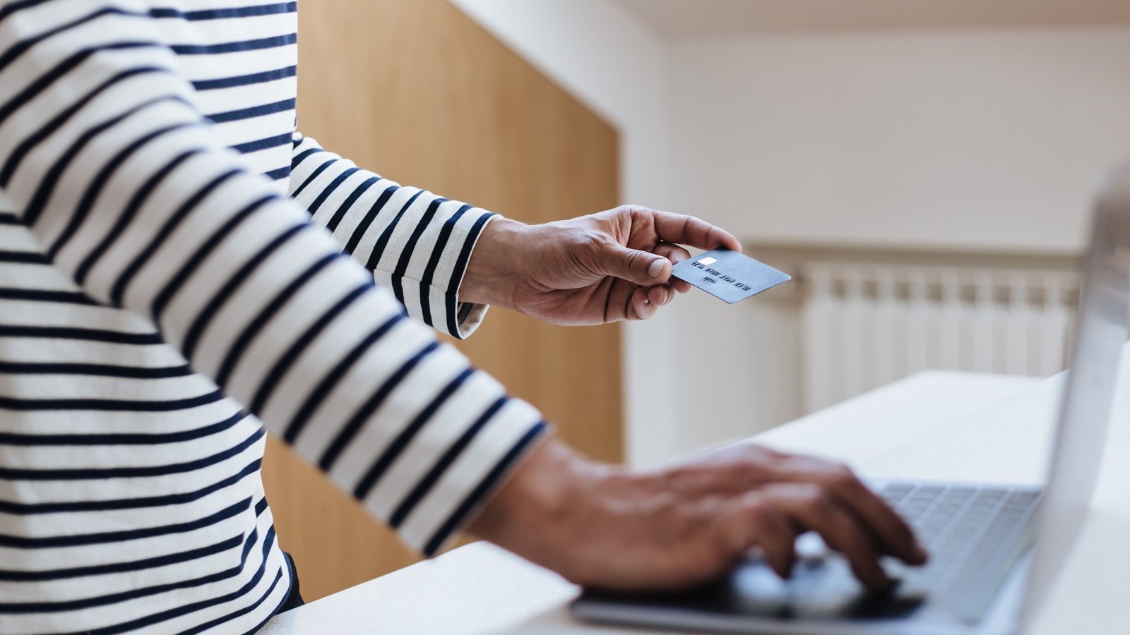 08 ach Personne en pull rayé tendant une carte bancaire en tapant sur un clavier