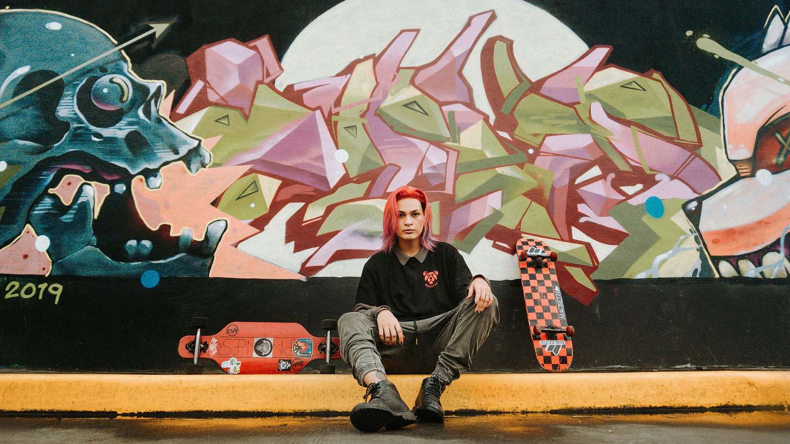 Skateur assis devant une fresque murale, planches posées à côté