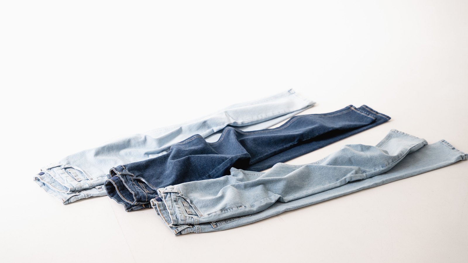 09 jea Trois jeans de délavages différents disposés à plat sur un fond clair